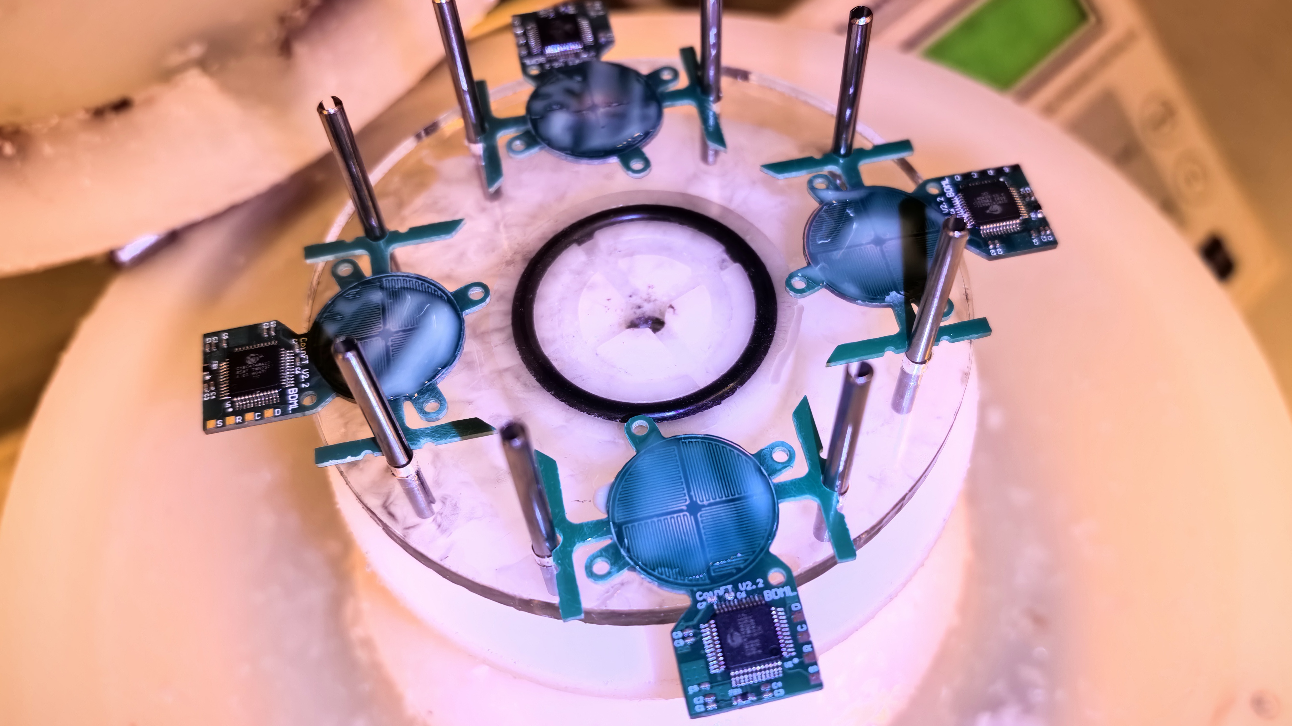 Four coin-sized CoinFT sensor boards mounted on a clear circular platform in the lab