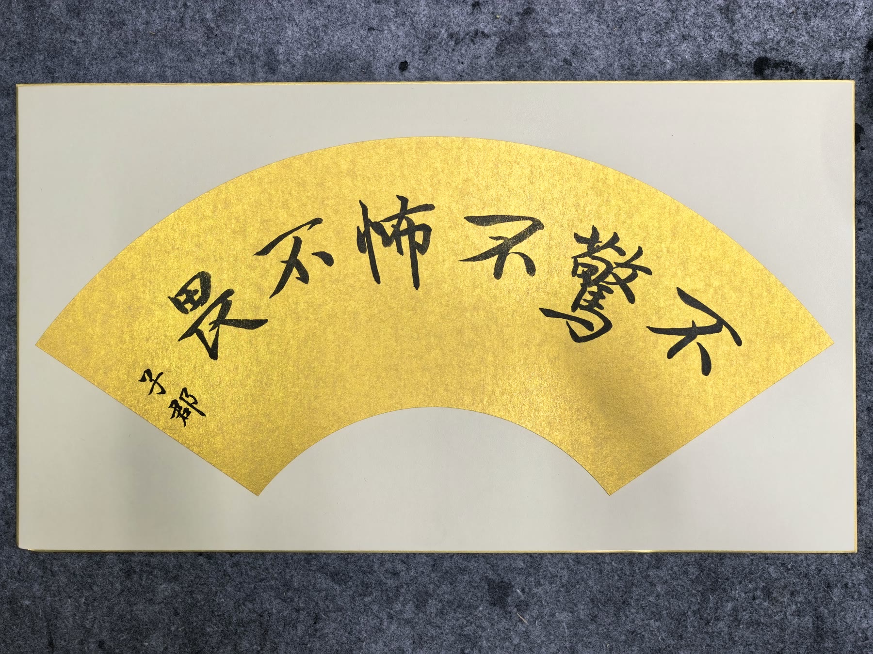Chinese calligraphy written in an arc across a gold fan shape