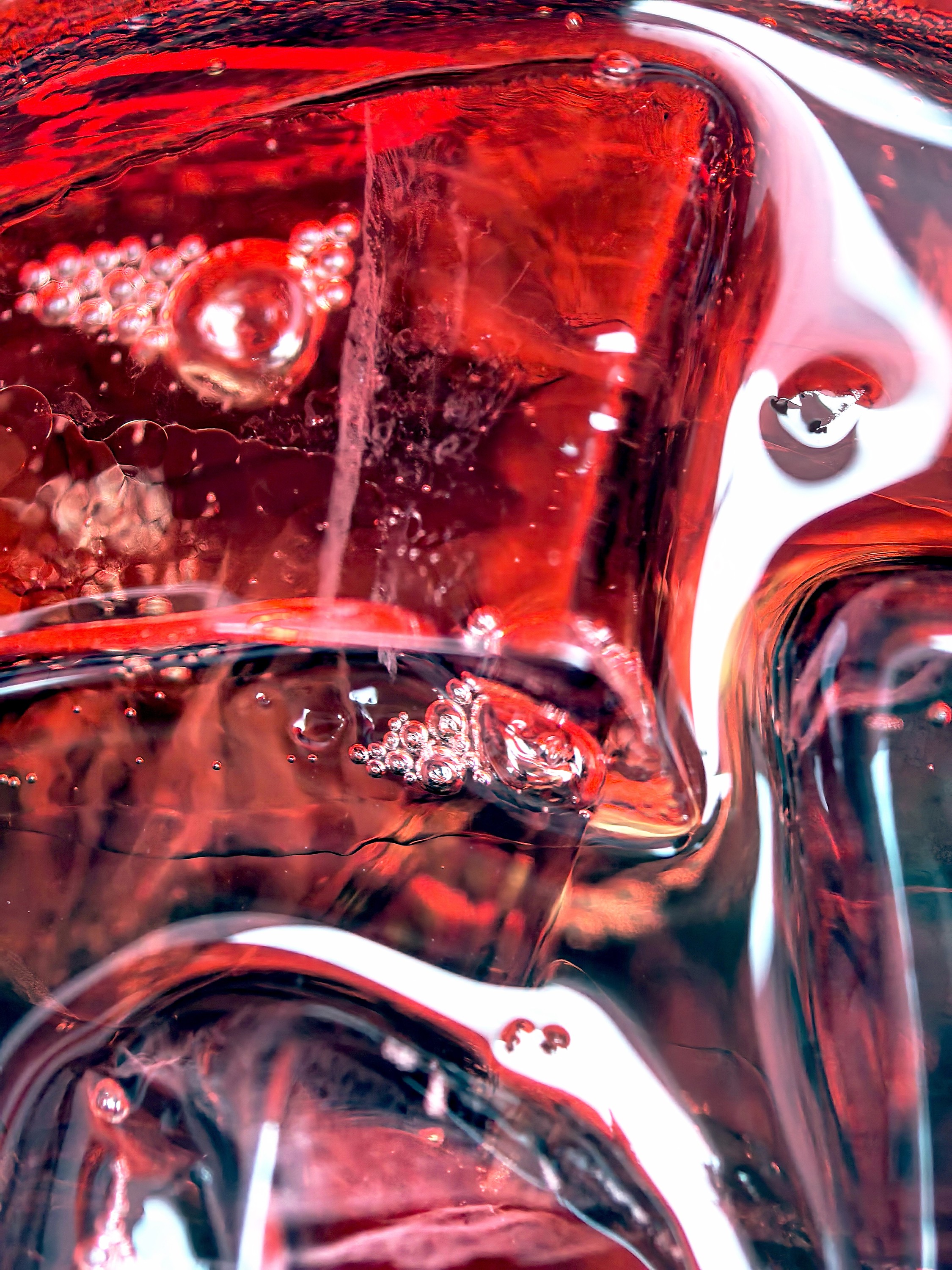 Close view of ice and bubbles refracting in dark red liquid